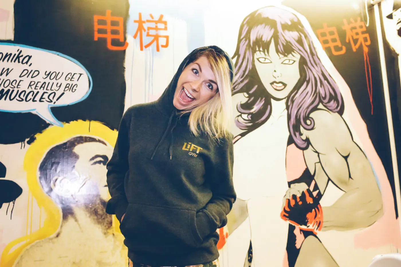A LiFT member in a branded hoodie posing beside the comic-style mural